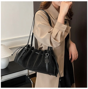 Detail of black pleated shoulder tote bag with drawstring and dual straps on beige coat