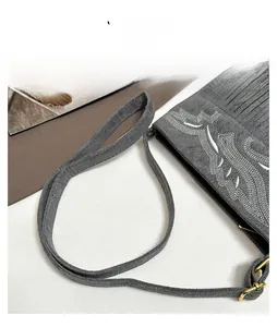 Detail of grey suede shoulder bag featuring white embroidery and bohemian fringe design
