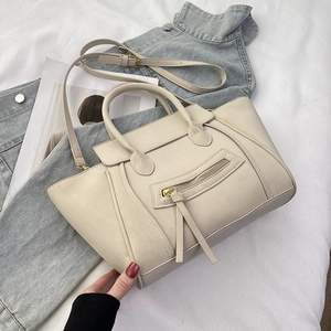 Detailaufnahme der cremefarbenen Trapez-Handtasche mit markanten Ziernähten und Quasten