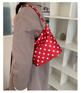Detailed view of red polka dot nylon handbag worn over shoulder on stylish trench coat