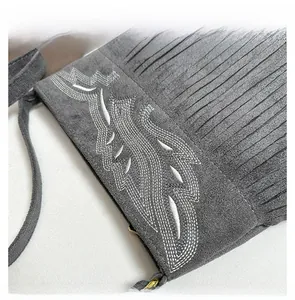 Close-up of gray suede bag featuring detailed wavy white embroidery and stylish fringe trim
