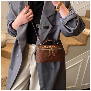 Detail of a brown quilted mini box bag with gold double zippers and top handle