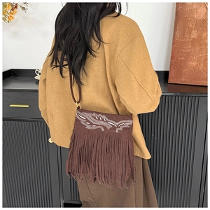 Detail of brown faux suede crossbody bag featuring leaf embroidery and long fringe tassels