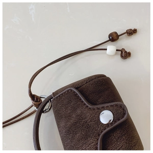 Detail of brown faux leather mini pouch with snap closure and beaded lanyard strap