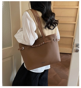 Détail d'un cabas en cuir marron montrant le grain et la boucle portés sur modèle