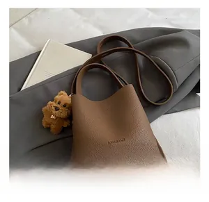 Detailed shot of a brown pebbled leather bucket bag with a cute plush bear charm accessory