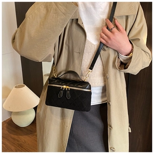 Close-up of a black quilted crossbody bag with gold hardware and a metal handle