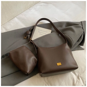 Détail du sac seau en cuir marron avec plaque dorée et mini pochette assortie