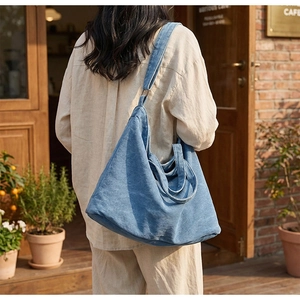 Détail d'un grand sac fourre-tout en denim bleu avec large bandoulière dans un café en plein air