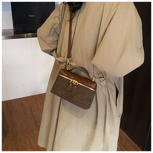 Detail of a dark brown quilted crossbody bag with dual zippers on a trench coat model