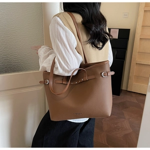 Sac cabas marron en cuir grainé avec boucle argentée porté à l'épaule par un mannequin