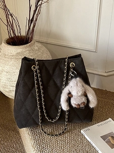Sac cabas matelassé noir avec chaîne dorée et pendentif lapin dans un décor minimaliste