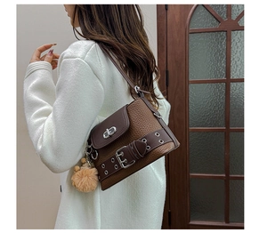 Détail d'un sac à bandoulière marron grainé avec boucle argentée et pompon décoratif