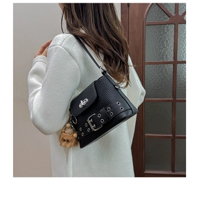Détail d'un sac à bandoulière en cuir grainé noir avec œillets et breloque ours