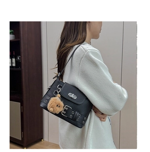 Détail d'un sac à bandoulière en cuir grainé noir avec sangles biker et petit ours