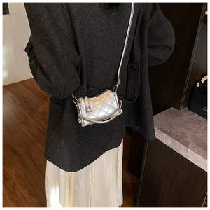 Detail of silver quilted mini crossbody bag worn by model with dark coat and pleated skirt