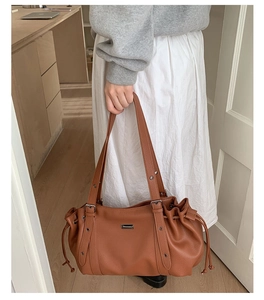 Detail of a brown lychee pattern leather tote bag featuring drawstring sides and rivets