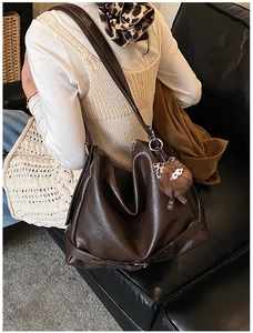 Detail of dark brown faux leather tote bag with plush charm on a model's shoulder