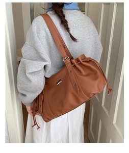Detail of a brown drawstring tote bag in pebbled leather with a silver metal plaque