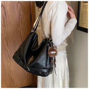 Close-up of a black soft leather shoulder bag with buckle details and a plush charm