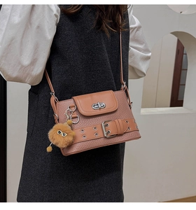 Détail du sac à bandoulière en cuir marron avec fermoir argenté et breloque en peluche
