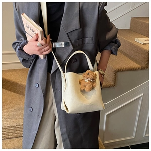 Chic beige lychee leather bucket bag with a cute plush bear pendant accessory