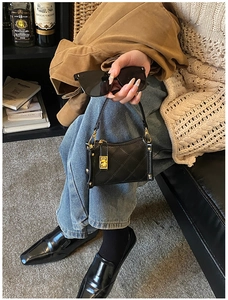 Detailed view of black quilted faux leather handbag with golden rectangular lock closure
