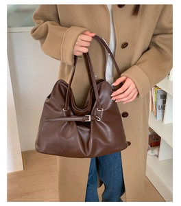 Detail of dark brown leather tote bag with buckle straps and side pleats held by a model