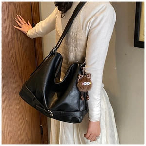Detail of a black glossy leather tote bag with a brown fuzzy charm and strap accents