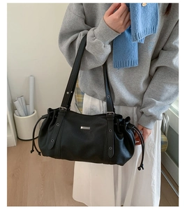 Detail of black pebbled leather tote bag with silver logo plate and side drawstrings