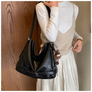 Detail of a large black leather tote bag with side buckles and a brown plush monster charm