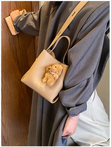 Detail view of beige lychee leather bucket bag with brand logo and cute bear charm