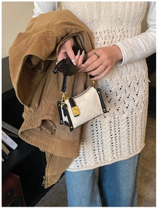 Detail of quilted beige handbag featuring contrast black edges and gold metal buckle