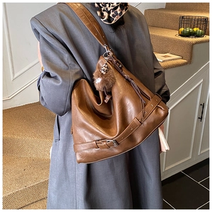 Close-up of a large brown vintage shoulder bag with buckle details and a plush charm