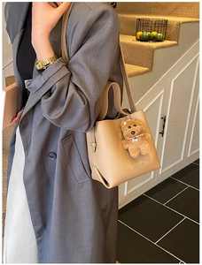 Detail of light brown bucket bag with lychee texture and plush bear pendant accessory