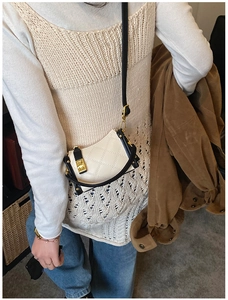Detail shot of the quilted beige mini bag with black trim and gold clasp on a model