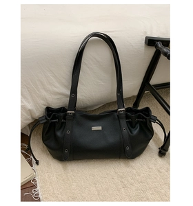 Detail of black pebbled tote bag with silver metal plate and side drawstring accents