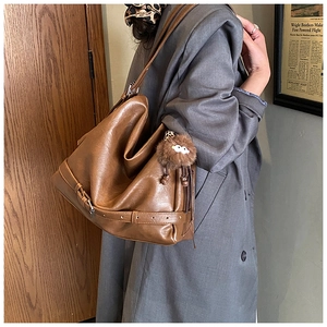 Detail view of large brown vintage motorcycle bag with fuzzy charm on model in gray coat