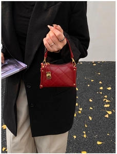Detail view of burgundy quilted mini handbag with gold-tone hardware on autumn street background