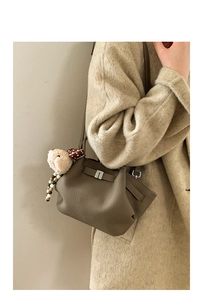 Brown lychee leather handbag detail with silver clasp and plush lamb charm on a beige coat
