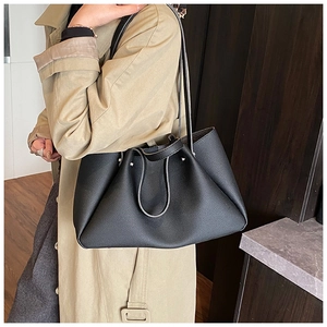 Side view of black leather tote bag with pleated folds on a khaki trench coat model