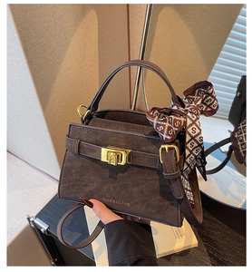 Detail of dark brown matte leather handbag featuring a gold turn-lock and silk scarf handle