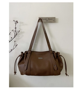 Detail of a brown lychee pattern leather tote bag with drawstring sides and decorative straps