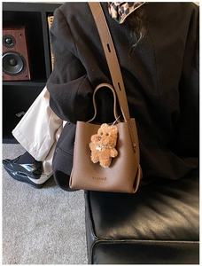 Close-up of brown litchi pattern leather bucket bag with a plush puppy keychain accessory