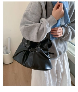 Detail of black pleated faux leather handbag with drawstring and silver metal rings