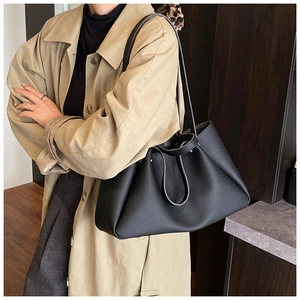 Detail view of large black leather tote bag with long straps on a female model in a trench coat