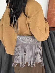 Gray faux suede crossbody bag with long tassels and white leaf embroidery on model