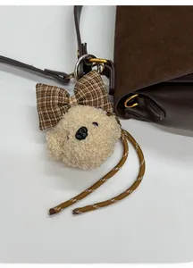 Detail view of a plush dog bag charm with a brown plaid bow on a leather bag