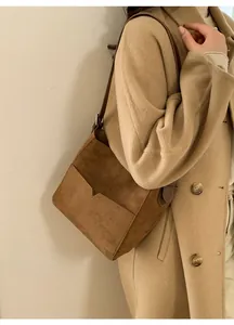 Vue latérale du sac seau en daim marron foncé avec bandoulière sur un manteau