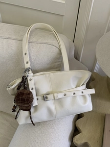 White vintage tote bag with metal eyelets and checkered cap charm on a sofa